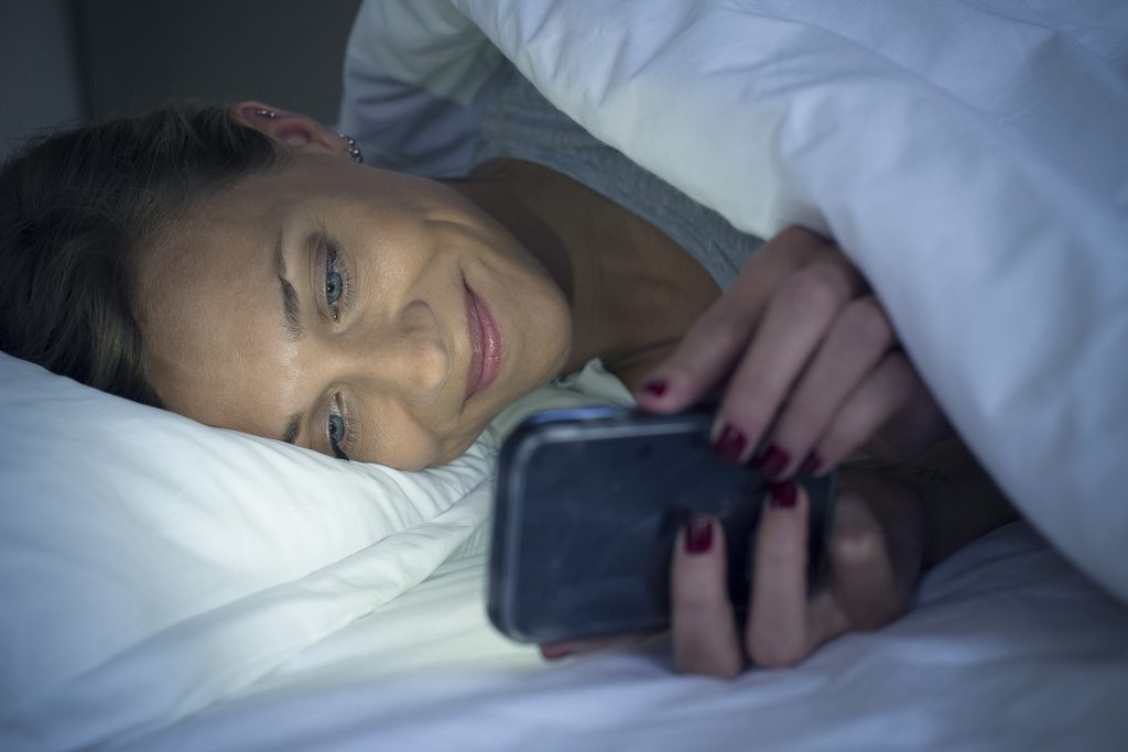 Kvinde ligger i sin seng og bruger netdating på sin iPhone.
